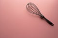 Single grey whisk at the top right of a plain pastel pink background