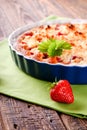 Single harvested strawberry in front of fruit pie in blue bowl on green towel