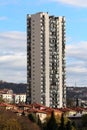 Single high skyscrapers rising above multiple family houses and smaller buildings on side of small hill surrounded with cloudy