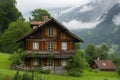 A single house stands in the middle of a vast field with majestic mountains visible in the distance, A quaint Swiss chalet in the Royalty Free Stock Photo