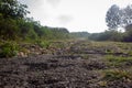 Single lane road with lot of potholes and cracked tarmac. Focus set on foreground gravel