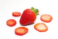 Single, large, fresh, red strawberry surrounded by sliced strawberries on a white surface Royalty Free Stock Photo