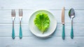 A single lettuce leaf rests delicately on a pristine plate, accompanied by a simple yet elegant place setting of cutlery on a Royalty Free Stock Photo