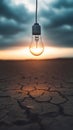 Lone light bulb suspended over parched, cracked ground, glowing warmly at sunset, representing resilience and breakthrough amid Royalty Free Stock Photo