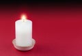 Single lit candle in gold rimmed white holder on red