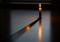 A single lit candle stands in a dimly lit setting, casting a warm glow and a long shadow on a Royalty Free Stock Photo
