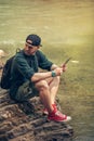 Single male hiker using tablet on nature while sitting on rocky river shore