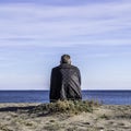 A single man sitting on an empty beach looking out to sea and blue sky with white clouds Royalty Free Stock Photo