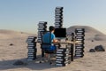 single man sitting at pc office workplace in desert environment with huge stacks of document binders workload stress burnout Royalty Free Stock Photo