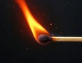 A single matchstick burns with bright orange and red flames against a dark background. Tiny sparks float around the lit match, Royalty Free Stock Photo