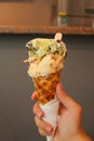 Single melting green and chocolate ice cream scoop flavor in waffle cone in hand holding on white Royalty Free Stock Photo