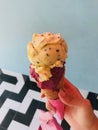 Single melting orange and purple ice cream scoop flavor in waffle cone in hand holding Royalty Free Stock Photo