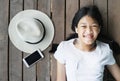 smiling Asia lying kid girl listen to the music by earphone with summer hat and mobile phone for summer relaxation on wood Royalty Free Stock Photo