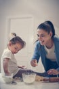 Single mother and little girl together in kitchen baking cookie.