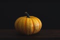 Single orange pumpkin against a black background on a brown board with room for copy space.