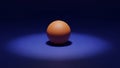 A single orange sits on a dark blue surface illuminated by a soft spotlight Royalty Free Stock Photo