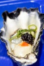 A single oyster live with garnish with an oyster shuck in the foreground with salmon roe