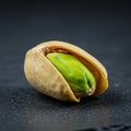 A single, partially opened pistachio nut is displayed on a dark surface. The outer shell Royalty Free Stock Photo
