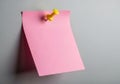 A single pink sticky note attached with a yellow thumbtack to a gray surface isolated on white background Royalty Free Stock Photo