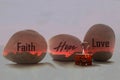 Positive word on three fire red stones - Faith Hope Love. With smiling paper clip on white table background. Spirituality concepts