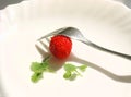 Single raw ripe strawberry on a white plate with mint leaves and a fork Royalty Free Stock Photo