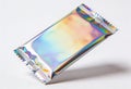 Shiny holographic foil wrapper with iridescent colors and serrated edges on a white background Royalty Free Stock Photo