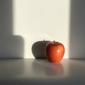 A single red apple is placed on a smooth, pale surface against a light beige wall. The Royalty Free Stock Photo