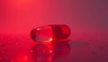 Single Red Pill Capsule Lying on Reflective Surface with Red Lighting Royalty Free Stock Photo