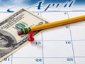 Single red pushpin on April 15 of calendar for tax income due date reminder on desktop with pencil and paper currency