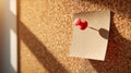 Single red pushpin securing a blank white note on a corkboard illuminated by warm natural light creating soft shadows and textured Royalty Free Stock Photo