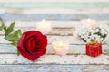 Single red rose, gift box, candles, and white flowers on turquoise table Royalty Free Stock Photo