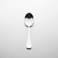 A single reflective metal spoon is set against a plain light colored backgroun Royalty Free Stock Photo