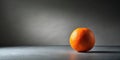 A single ripe orange rests on a sleek, grey surface against a muted background, illuminated by a soft, diffused light. Generative Royalty Free Stock Photo