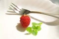 Single  ripe strawberry on a white plate with mint leaves and a fork Royalty Free Stock Photo