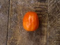 A single ripe tomato with a smooth, shiny surface sits on a rustic, textured wooden table. Royalty Free Stock Photo