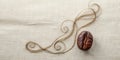 A single roasted coffee bean rests beside a decorative twine design on a textured beige fabric. Generative AI Royalty Free Stock Photo