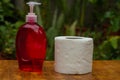 Single roll of white toilet paper and Pump bottle of red soap on wood desk table Royalty Free Stock Photo