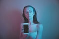 Single sad teen holding a mobile phone lamenting sitting on the bed in her bedroom with a dark light in the background Royalty Free Stock Photo