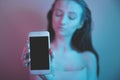 Single sad teen holding a mobile phone lamenting sitting on the bed in her bedroom with a dark light in the background Royalty Free Stock Photo