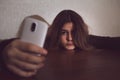 Single sad teen holding a mobile phone lamenting sitting on the bed in her bedroom with a dark light Royalty Free Stock Photo