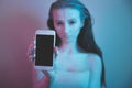 Single sad teen holding a mobile phone lamenting sitting on the bed in her bedroom with a dark light in the background Royalty Free Stock Photo