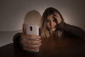 Single sad teen holding a mobile phone lamenting sitting on the bed in her bedroom with a dark light Royalty Free Stock Photo