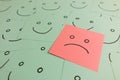 Single sad unhappy face emoticon among happy smiling ones