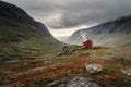 A single small red cabin billows smoke from it`s tiny chimney in the remote gorge of central Norway. The distant dark clouds give Royalty Free Stock Photo