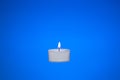 Single small white candle burning. Close up studio shot, isolated on blue background Royalty Free Stock Photo