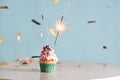 Single sparkler on cupcake blue wall.