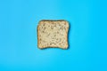 Single square piece of bread with seeds for toast lies on blue table on kitchen. Top view