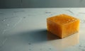 single, square-shaped orange object rests on white marble surface, casting shadow and reflecting the light. Royalty Free Stock Photo