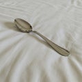 A single stainless steel spoon with a smooth, reflective surface is placed on a white, Royalty Free Stock Photo
