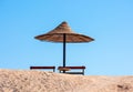 Single sun parasol and seating bench against a blue sky.